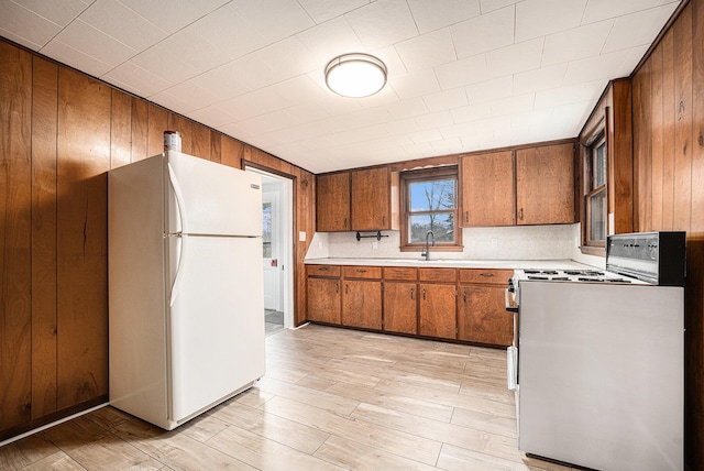 kitchen with light countertops, wooden walls, white appliances, light wood-style flooring, and brown cabinetry
