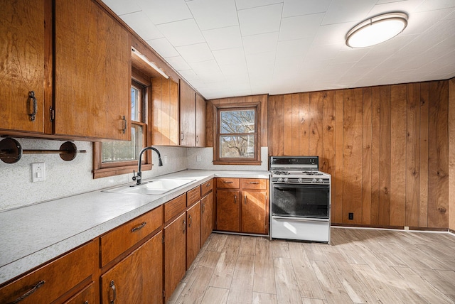 kitchen with light countertops, a sink, light wood-style floors, range with gas stovetop, and brown cabinetry