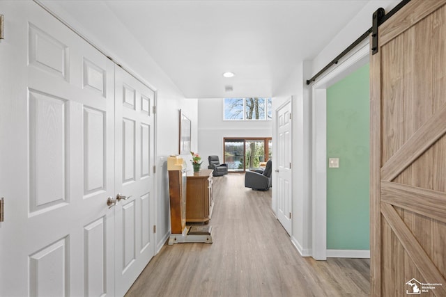 hall with light wood-style flooring, baseboards, recessed lighting, and a barn door