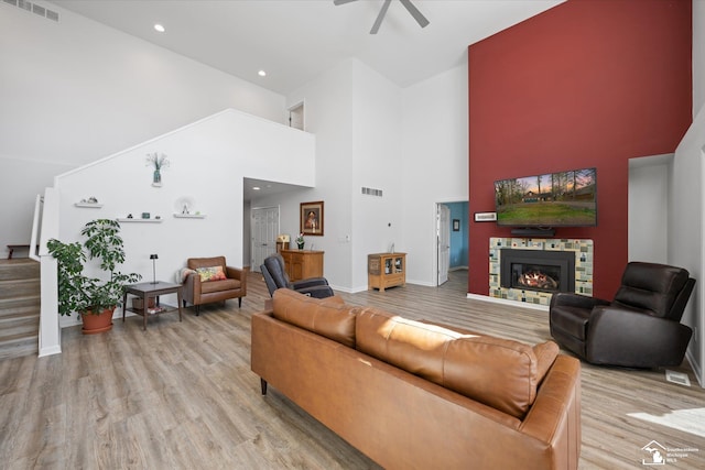 living room with visible vents, light wood-style flooring, a high ceiling, and ceiling fan