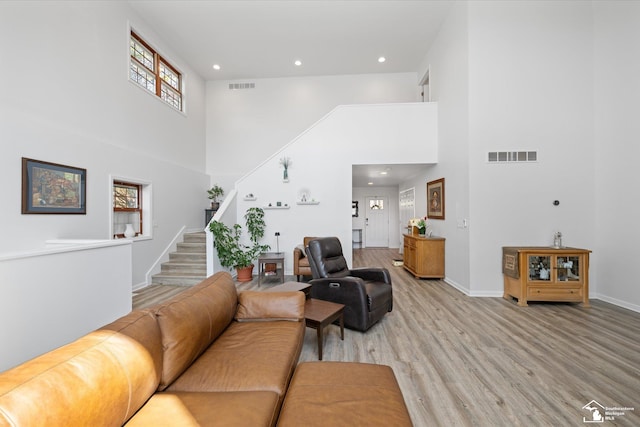 living area with stairway, visible vents, light wood finished floors, and a high ceiling