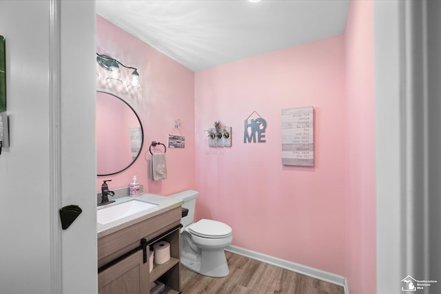 half bath featuring toilet, vanity, wood finished floors, and baseboards