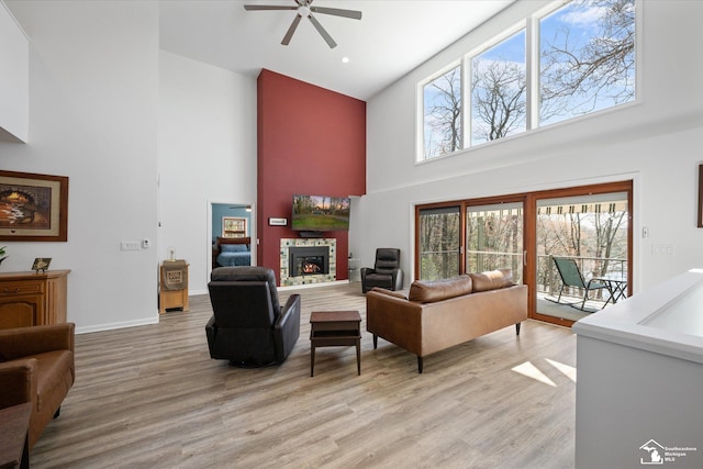 living area featuring light wood finished floors, a ceiling fan, baseboards, a fireplace, and high vaulted ceiling