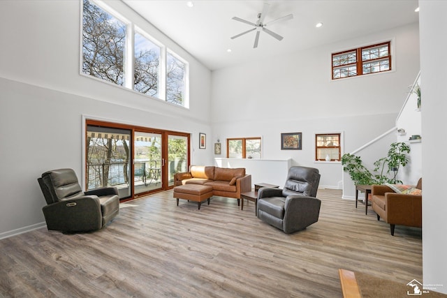 living room with a ceiling fan, wood finished floors, a high ceiling, baseboards, and recessed lighting