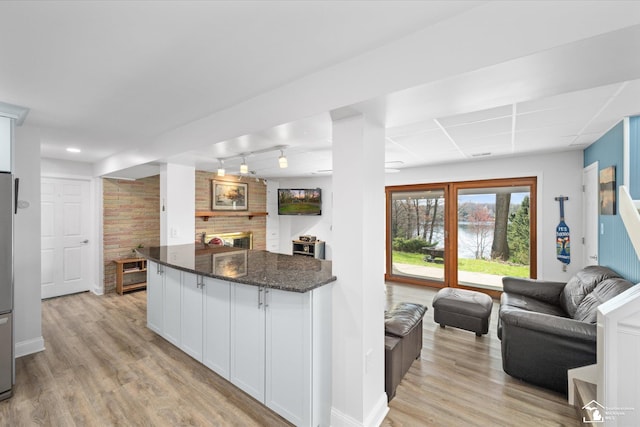 kitchen with dark stone counters, open floor plan, white cabinetry, and light wood-type flooring