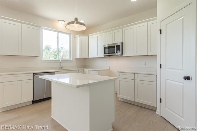 kitchen featuring white cabinets, a sink, decorative light fixtures, a kitchen island, and appliances with stainless steel finishes