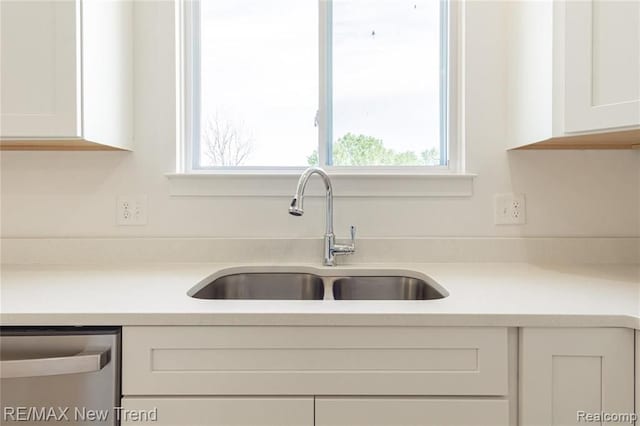 kitchen featuring plenty of natural light, dishwasher, a sink, and white cabinetry