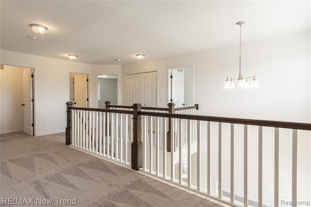 hallway featuring baseboards, carpet floors, and a chandelier