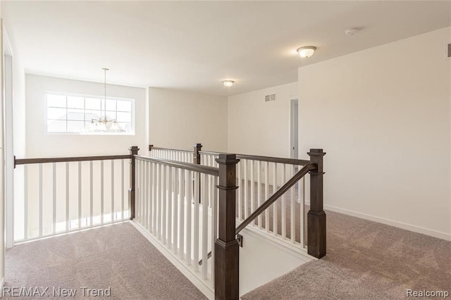 hallway featuring an upstairs landing, a chandelier, carpet floors, baseboards, and visible vents