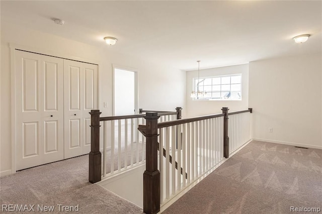 corridor with baseboards, a notable chandelier, an upstairs landing, and carpet