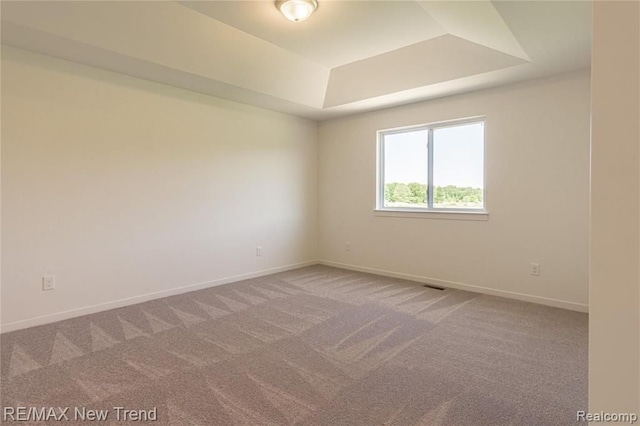 unfurnished room featuring a tray ceiling, carpet floors, and baseboards