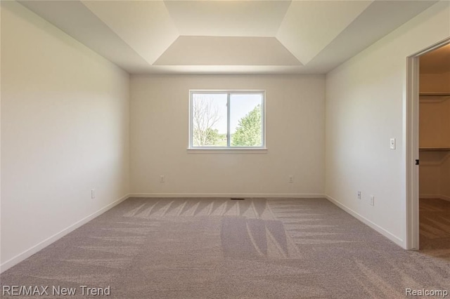 carpeted spare room featuring a tray ceiling and baseboards