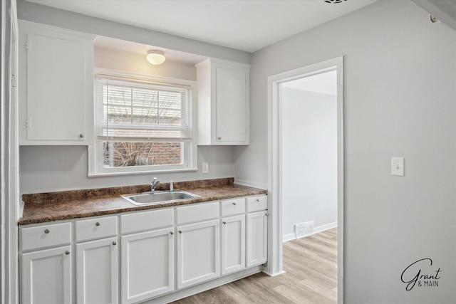 19931 Braile St, Detroit, MI 48219 - kitchen with dark countertops, a sink, light wood finished floors, white cabinetry, and visible vents