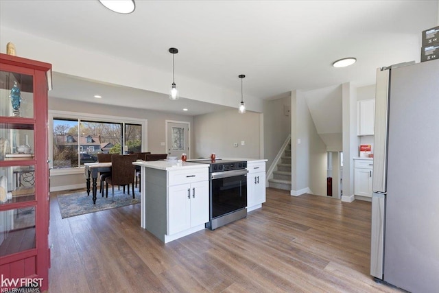 kitchen with light countertops, wood finished floors, freestanding refrigerator, electric range, and white cabinetry