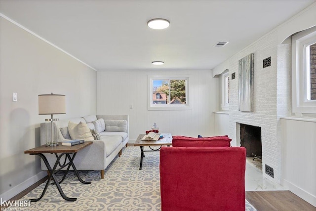 living area featuring baseboards, ornamental molding, a brick fireplace, and visible vents