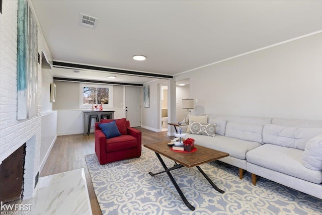 living room with a brick fireplace, wood finished floors, and visible vents