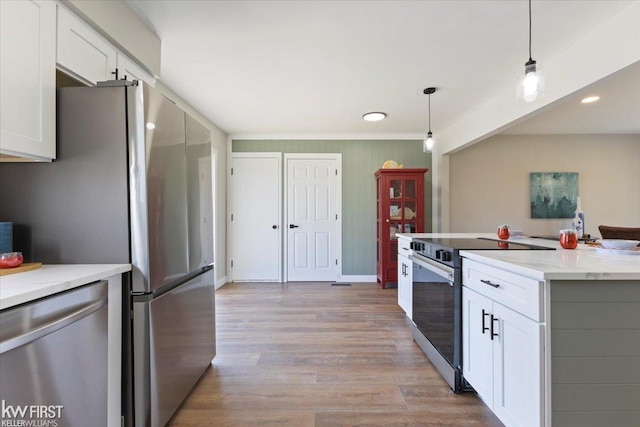 kitchen with light wood finished floors, stainless steel appliances, decorative light fixtures, and white cabinetry
