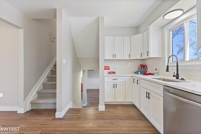 kitchen featuring white cabinets, stainless steel dishwasher, a sink, and light wood-style floors