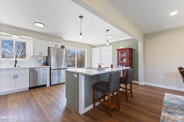 kitchen with a sink, stainless steel appliances, baseboards, white cabinetry, and dark wood-type flooring