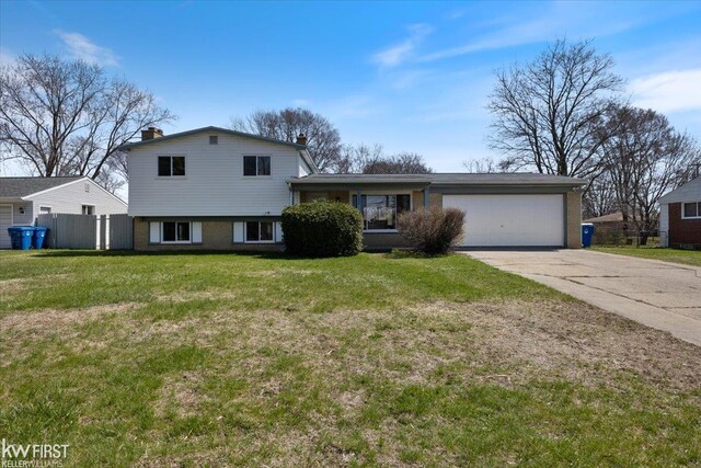 tri-level home with concrete driveway, a front lawn, a chimney, fence, and a garage