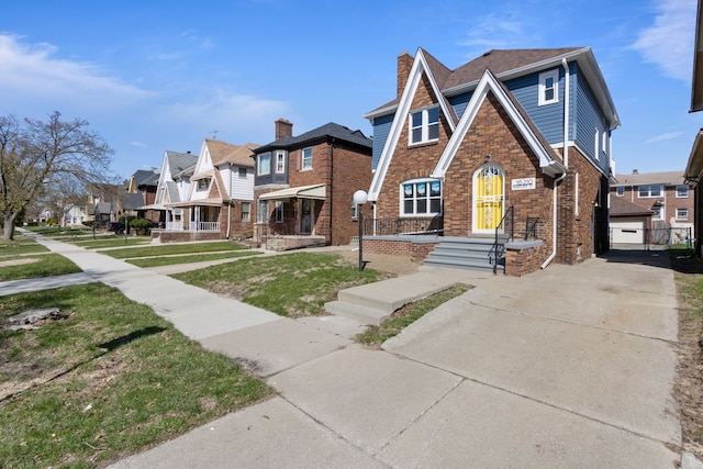 tudor-style house featuring a chimney, a residential view, driveway, brick siding, and a front yard