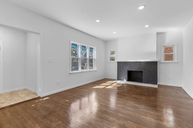 unfurnished living room featuring baseboards, wood finished floors, a brick fireplace, and recessed lighting