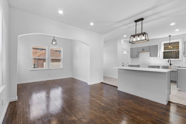 kitchen featuring arched walkways, backsplash, dark wood-type flooring, and gray cabinetry