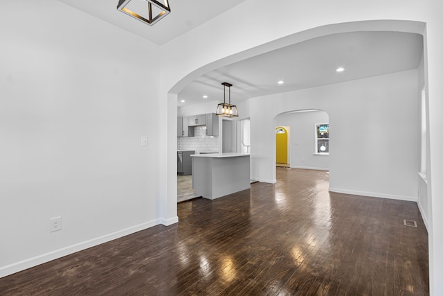 unfurnished living room with arched walkways, visible vents, baseboards, dark wood-style floors, and recessed lighting
