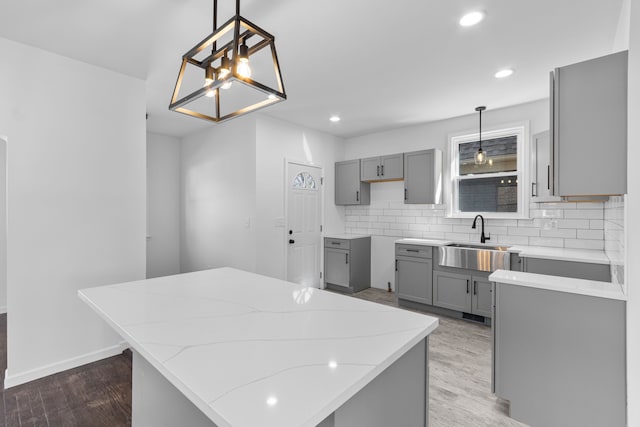 kitchen with a center island, wood finished floors, a sink, decorative backsplash, and gray cabinetry