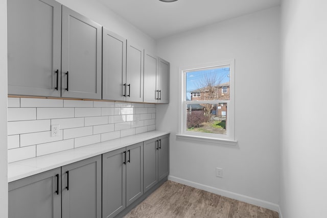 kitchen featuring light countertops, gray cabinets, light wood-style flooring, backsplash, and baseboards