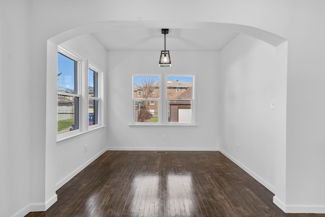 unfurnished dining area with arched walkways, baseboards, and hardwood / wood-style flooring