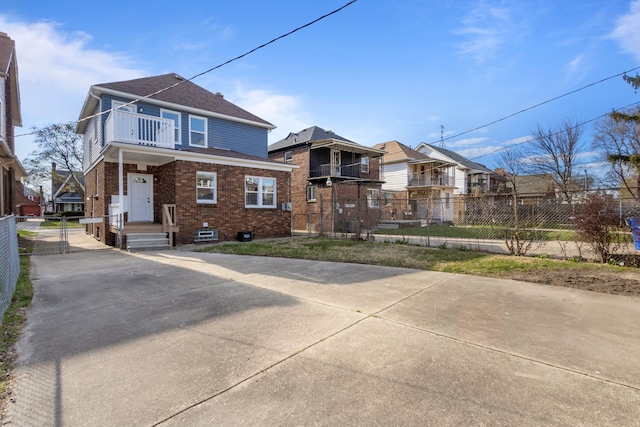 view of front of property featuring a residential view, driveway, fence, brick siding, and a balcony
