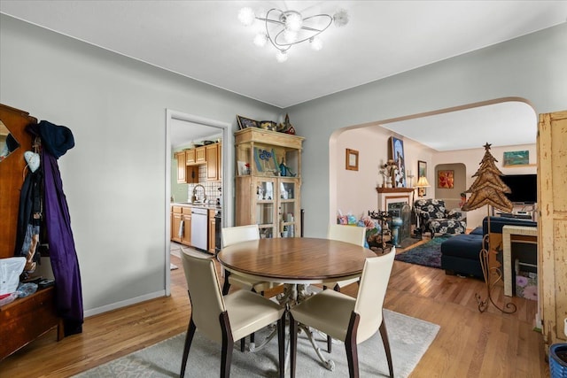 45520 Deshon St, Utica, MI 48317 - dining space featuring arched walkways, a fireplace, light wood finished floors, and an inviting chandelier