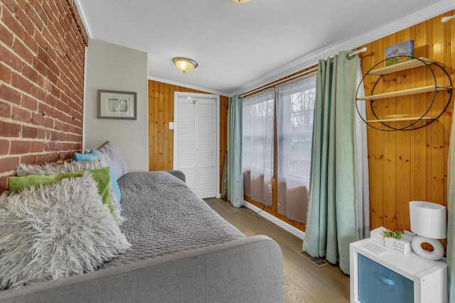 bedroom with wooden walls, vaulted ceiling, visible vents, wood finished floors, and brick wall