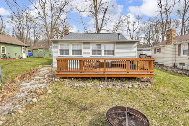 rear view of property with a chimney, a lawn, a fire pit, a wooden deck, and a storage unit