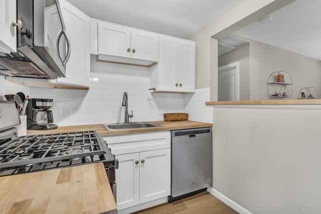 kitchen featuring wooden counters, backsplash, a sink, appliances with stainless steel finishes, and white cabinetry