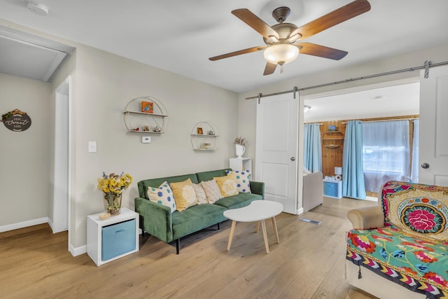 living room with a barn door, baseboards, a ceiling fan, and wood finished floors
