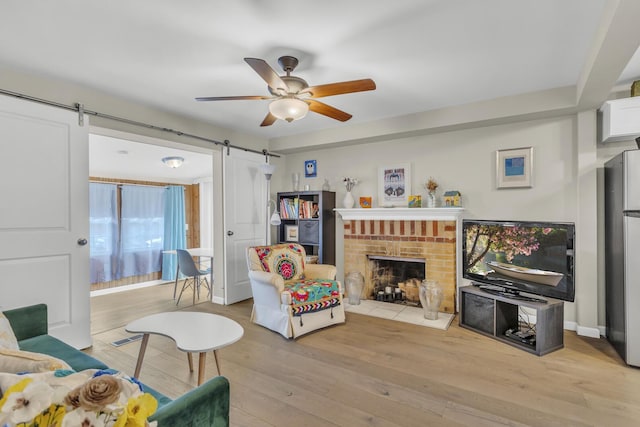living area with light wood finished floors, a barn door, visible vents, a ceiling fan, and a fireplace