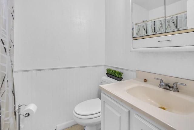 full bath featuring toilet, vanity, a wainscoted wall, and a shower with curtain