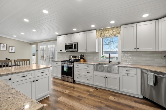 kitchen with backsplash, appliances with stainless steel finishes, a sink, and white cabinetry