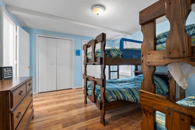 bedroom with a closet, light wood-style flooring, a textured ceiling, and baseboards