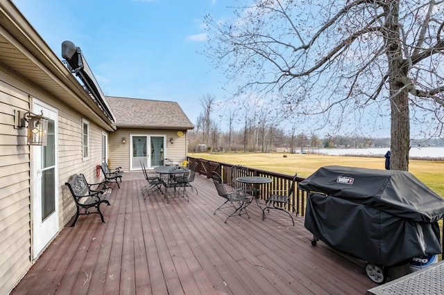 deck featuring a water view, outdoor dining space, a yard, and area for grilling