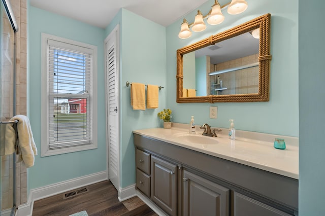 bathroom featuring a tile shower, baseboards, visible vents, wood finished floors, and vanity