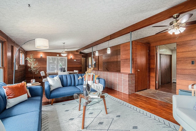 living room with a ceiling fan, wood finished floors, wooden walls, and a textured ceiling