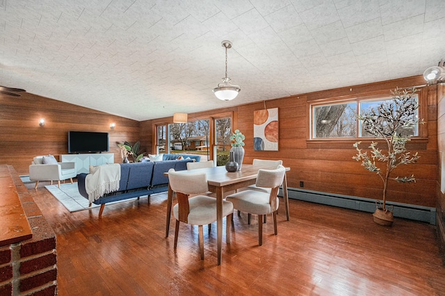 dining space featuring a baseboard heating unit, hardwood / wood-style floors, a healthy amount of sunlight, and wood walls