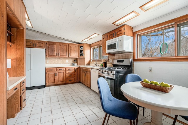 kitchen featuring brown cabinetry, backsplash, white appliances, and light countertops