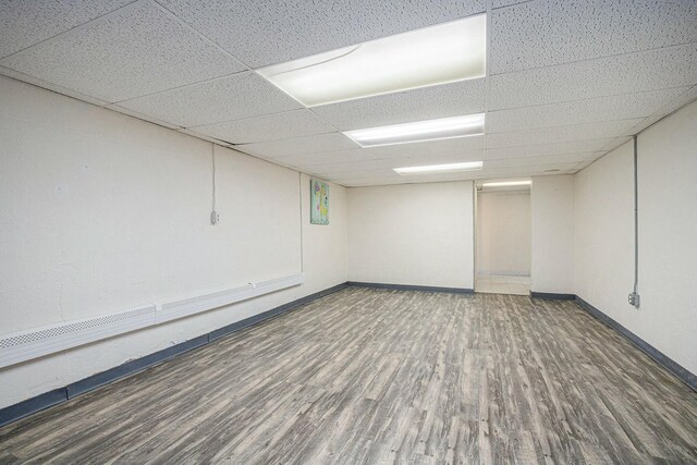 unfurnished room with baseboards, wood finished floors, and a drop ceiling