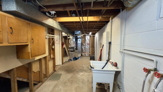 unfinished below grade area featuring concrete block wall, heating unit, and a sink