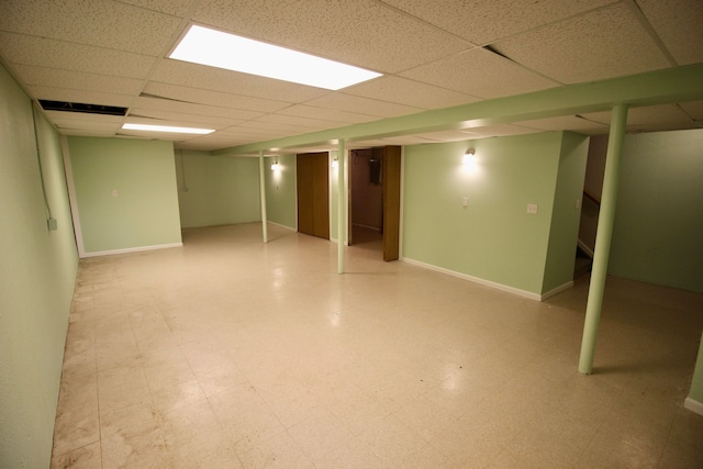 finished basement featuring a paneled ceiling, tile patterned floors, baseboards, and stairway