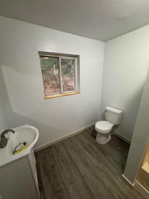 bathroom with toilet, vanity, wood finished floors, and baseboards